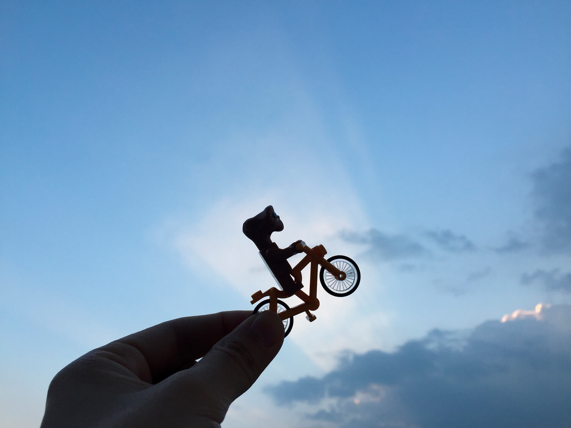 Uma mão branca segura uma miniatura de boneco em bicicleta em alusão à cena clássica do filme E.T.