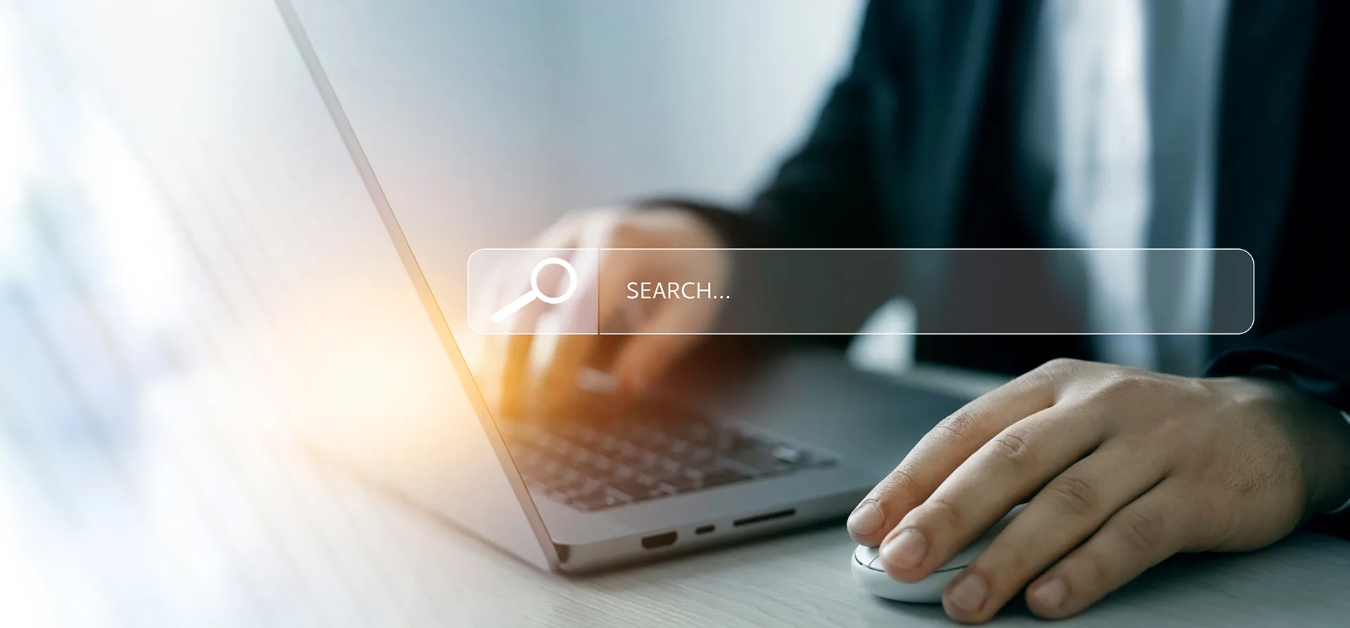 Homem de casaco preto está usando o computador. Na tela se vê uma ferramenta de busca “search”