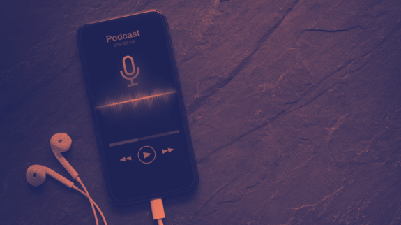 Smartphone exibindo player de podcast com ícone de microfone e ondas sonoras coloridas na tela, ao lado de fones de ouvido brancos.
