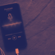 Smartphone exibindo player de podcast com ícone de microfone e ondas sonoras coloridas na tela, ao lado de fones de ouvido brancos.